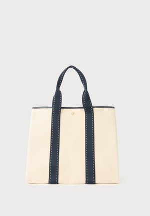 Krémová taška cez rameno s dvoma námornícky modrými rukoväťami so bielym prešívaním, obdĺžnikovým tvarom a malým zlatým logom v strede prednej strany.