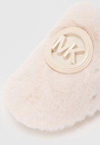 Lichtroze wollen pantoffel met een cirkelvormig crèmekleurig logo met de letters "MK" in reliëf. Zachte textuur en afgeronde vorm.