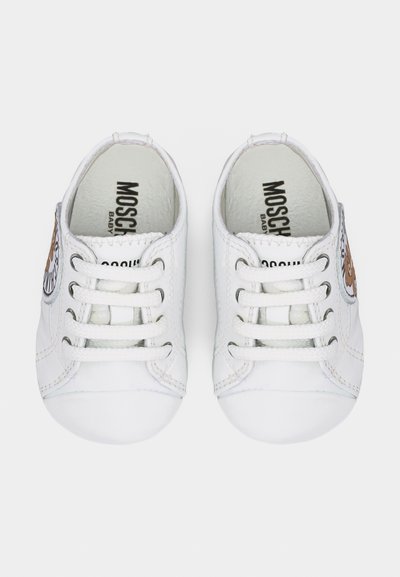 Ζευγάρι λευκά παπουτσάκια μωρού με κορδόνια, διακοσμημένα με κεντητά σχέδια αρκούδας στις πλευρές και τη φράση "MOSCHINO BABY" τυπωμένη στο εσωτερικό.