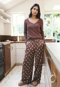 Camicia marrone a manica lunga con bottoni, abbinata a pantaloni marroni con motivo, dotati di leggeri motivi. Tessuto morbido e vestibilità rilassata.