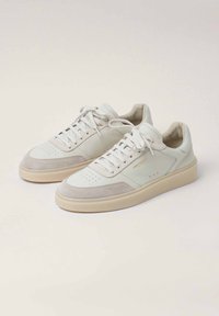 Weiße Ledersneaker mit hellgrauen Wildlederakzenten, durchlochter Zehenpartie, flachen Schnürsenkeln und einer cremefarbenen Gummisohle. Goldene Markierung an der Seite.