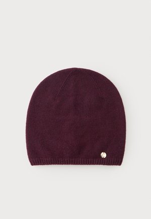 Bonnet en tricot violet foncé avec un petit emblème rond doré près du bord inférieur, présenté sur un fond clair uni.