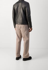 Schwarze Lederjacke mit Reißverschluss-Ärmeln, kombiniert mit hellbeigen, lässigen Hosen und strukturierten schwarzen Schuhen. Die Rückansicht zeigt detaillierte Nähte.