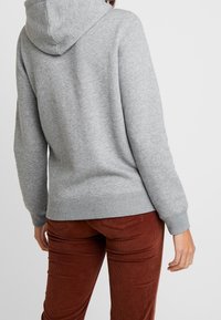 Grå huvtröja med strukturerad yta, elastiska ärmslut och nederkant. I kombination med bruna cordjackor, visas i sid- och bakvy.