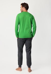 Camisa de manga larga verde combinada con pantalones gris oscuro que presentan un patrón verde repetido. Tejido suave, corte casual y puños elásticos.