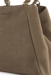 Brązowa torebka ze zamszu o miękkiej fakturze, o wyraźnym kształcie i złotych akcentach. Logo wytłoczone na boku.