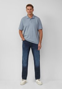 Hellgraues Poloshirt mit Kragen, kombiniert mit dunkelblauen Jeans und cremefarbenen Sneakers. Glatter Stoff, einfaches Design und gerade Passform.