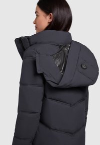 Donkergrijze gewatteerde jas met een hoge kraag, lichtgewicht stof, een doorgestikte design en een contrasterende glanzende binnenvoering. Voorzien van een knoopdetail.