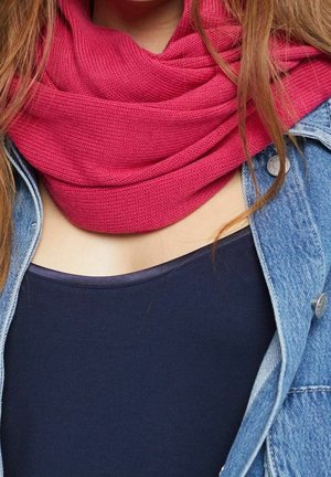 Femme portant une écharpe tricotée rose vif sur un haut foncé et une veste en denim bleue, avec de longs cheveux tombant autour de son cou et de ses épaules.