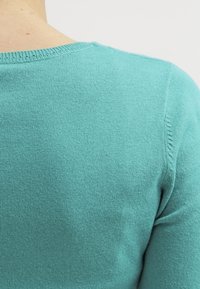 Turkos tröja med en mjuk textur, rund halsringning och sömlösa axeldetaljer, lämplig för avslappnad användning.