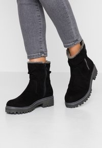 Bottines en suède noir avec un doux revers en fausse fourrure grise et un détail de fermeture éclair. Les semelles épaisses et texturées offrent adhérence et stabilité.