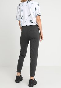 Gray tapered pants with a smooth texture, featuring side pockets, paired with a white and black tie-dye t-shirt and black sneakers.