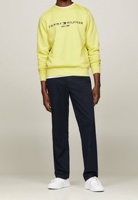 Žlutá mikina s logem "TOMMY HILFIGER EST. 1985", doplněná tmavě modrými kalhotami a bílými teniskami. Ležérní střih, žebrované manžety, hladká struktura.