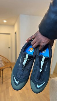 Black Nike Air Max shoes with a smooth upper, zipper closure, green accents on the sole, and a blue insole.