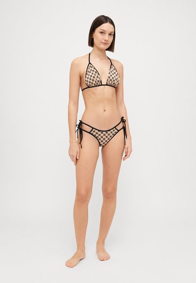 Bikini komplekts ar rakstainu trīsstūra augšdaļu un saites apakšdaļā, smilšu krāsā ar melniem akcentiem. Materiāls izskatās mīksts un elastīgs.