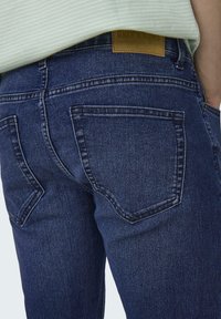 Mørkeblå denimjeans med et klassisk fem-lomme design, med en subtil farvefading og en brun læderlogo-patch på taljen.