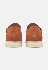 Scarpe brown in suede con un design arrotondato e una suola bassa color crema. Presentano un dettaglio con fibbia laterale con una finitura текстurizzata.