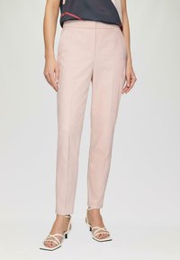 Pantalons sur mesure rose clair avec une coupe ajustée, dotés d'une texture lisse, d'un design épuré et de détails minimalistes. Associés à des talons blancs à brides.