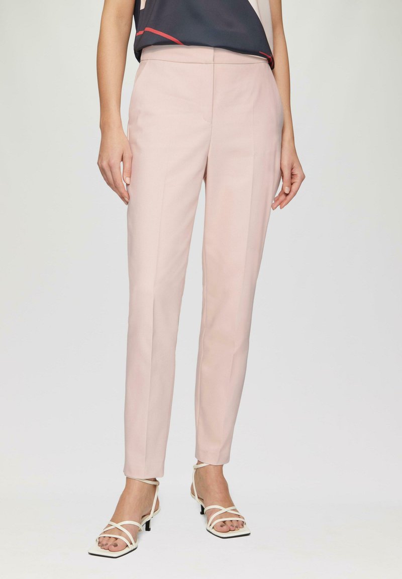 Pantalons sur mesure rose clair avec une coupe ajustée, dotés d'une texture lisse, d'un design épuré et de détails minimalistes. Associés à des talons blancs à brides.
