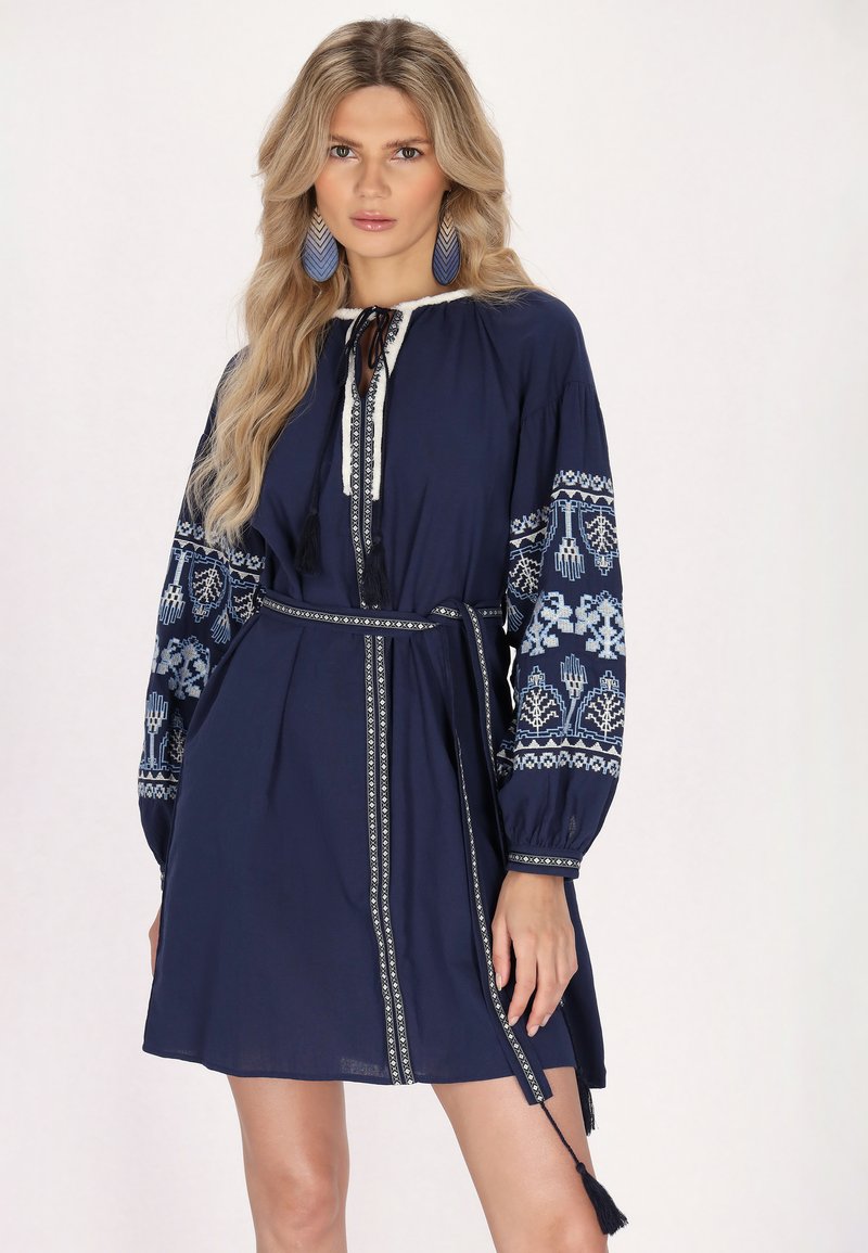 Marineblaues Kleid mit bestickten langen Ärmeln, einem Kordelzug-Halsausschnitt und einem passenden Gürtel. Verfügt über Quastenakzente und dekorative Borten.