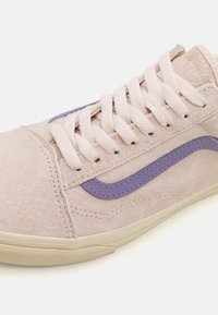Sneaker en suède rose clair avec de grosses lacets et une bande latérale violette, semelle beige, gros plan sur le laçage et le dessus.