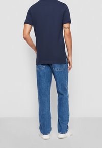 Marinblå t-shirt med kort ärm och rundad halsringning, matchad med ljusblå denimjeans. Vita sneakers fulländar outfiten.