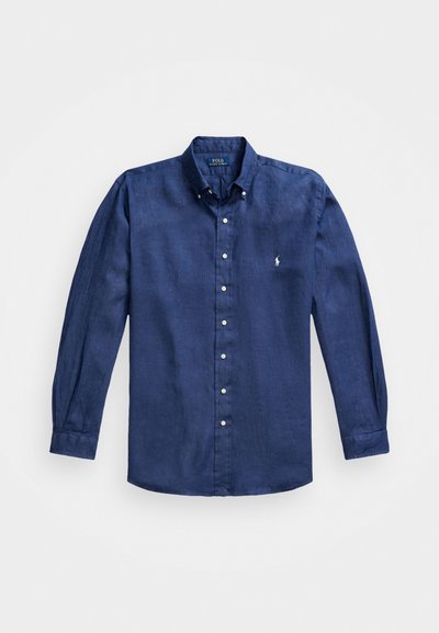 Mörkblå långärmad skjorta i linne, med krage som knäpps ned, vita knappar och en liten broderad logga på bröstet.