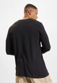 Zwarte lange mouwen shirt met een gladde textuur, ronde halslijn en een relaxte pasvorm, weergegeven vanuit de achterkant tegen een effen achtergrond.