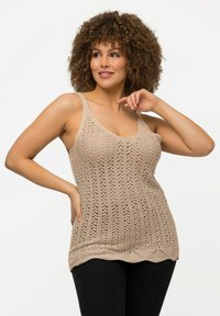 Top a canotta lavorato a maglia beige con un motivo all'uncinetto, caratterizzato da spalline larghe e orlo scallop, abbinato a pantaloni neri aderenti.