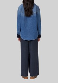 Camicia di jeans con parte superiore di un blu più chiaro e parte inferiore di un blu più scuro, caratterizzata da maniche lunghe con polsini bottonati, abbinata a pantaloni a gamba larga color navy.