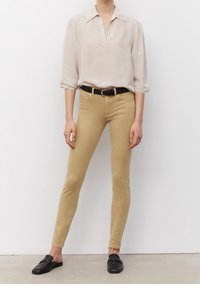 Beige přiléhavé džíny v kombinaci s krémovou blůzou s límečkem a krátkými rukávy, doplněné černým opaskem a černými mokasíny.