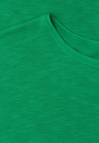 Tissu tricoté vert avec un gros plan sur une encolure arrondie et des coutures visibles le long du bord du col.