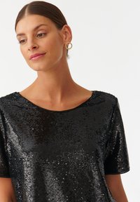 Top nero con paillettes, scollo rotondo e maniche corte, caratterizzato da una texture liscia e una superficie lucida e riflettente.