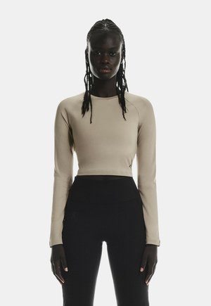 Beige long-sleeve crop top made of a smooth, stretchy material, paired with high-waisted black leggings featuring a logo detail.