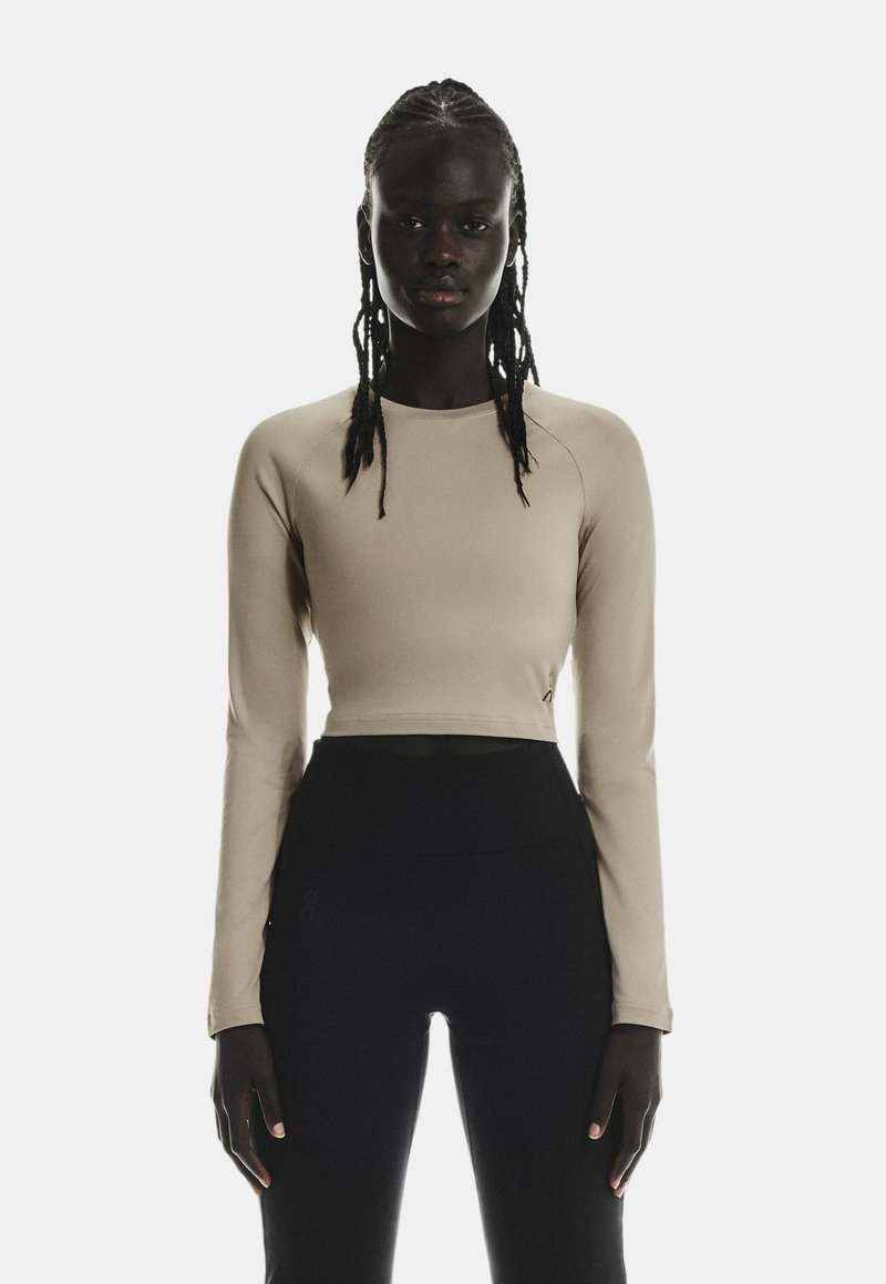 Un crop top beige à manches longues fabriqué dans un matériau lisse et extensible, associé à des leggings noirs taille haute avec un détail de logo.