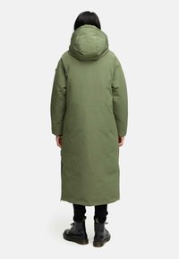 Lang olivenfarvet parka med h�ætte, der har en glat ydre tekstur og to sidelommer med lynlås. Båret over sorte bukser og støvler.
