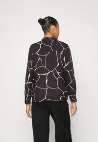 Blouse noire avec un motif abstrait beige clair, à manches longues et col, conçue avec une coupe décontractée et un tissu doux.