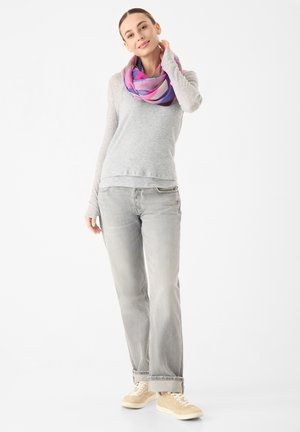 Chemise à manches longues gris clair et jeans gris, associés à une écharpe nouée colorée dans des tons de rose et de violet, portée avec des baskets beiges.