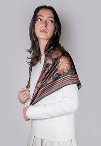 Pañuelo de seda con un patrón floral en tonos cálidos sobre un fondo oscuro, bordado con rayas marrones y naranjas.