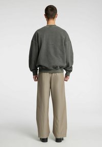 Felpa grigia oversize con spalle scese, polsini e orlo a costine. Abbinata a pantaloni beige a gamba larga e scarpe nere. Marchio minimale visibile.