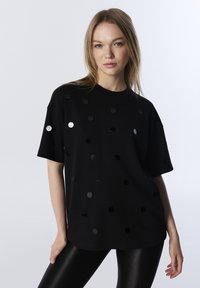 Czarna koszulka z krótkim rękawem z połyskujących czarnych i srebrnych okrągłych cekinów ułożonych w kropkowy wzór na przodzie.