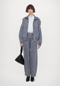 Jachetă din denim gri supradimensionată cu manșete ribbate, cămașă polo albastră deschisă, pantaloni din denim gri lărgiți și geantă din piele ecologică neagră.