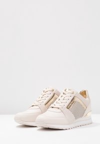 Beige sneakers with mesh panels, gold accents, and laces. Featuring a rounded toe and a textured sole for grip and durability.