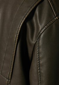 Mörkbrun läderjacka med axeldetaljer, som har en slät textur, synliga sömmar och en avslappnad passform.