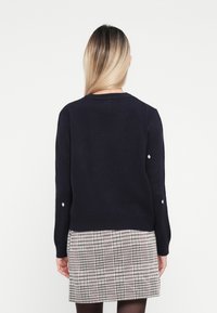 Navy knit sweater with a round neckline and long sleeves, featuring subtle dot details on the sleeves, paired with a patterned skirt.