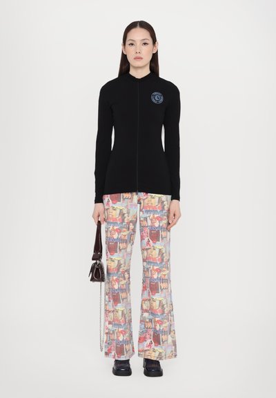 Top negro de manga larga con cremallera, diseño ajustado; pantalones acampanados coloridos impresos con diversas imágenes y palabras; combinados con un bolso pequeño.
