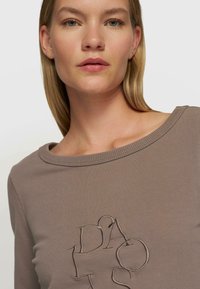 Sweatshirt taupe surdimensionné avec un col rond et des lettres brodées dans une couleur contrastante sur le devant. Texture douce.