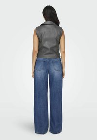 Graue ärmellose Lederweste kombiniert mit hoch taillierten, weit geschnittenen blauen Jeans, die über eine glatte Textur und ein klassisches Five-Pocket-Design verfügen.