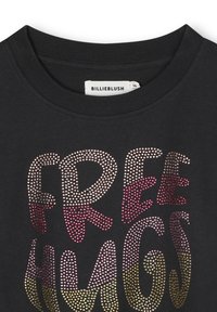 T-shirt noir avec le texte "FREE HUGS" en rhinestones scintillants, avec un effet dégradé allant du rose à l'or. Design classique à col rond.