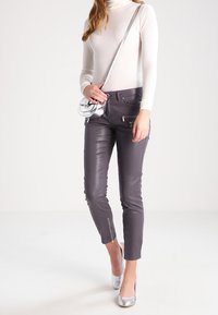 Pantalones de cuero gris con un diseño ajustado, cremalleras en los tobillos y una textura suave. Combinados con un suéter de cuello alto color crema y tacones plateados.